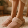 elegant woman wearing soft blush pink best slippers for women on white fluffy rug in cozy room